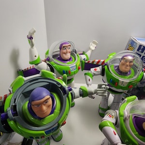 May include: A collection of five green, white, and purple Buzz Lightyear action figures from the Toy Story franchise. The figures are all in different poses, with some of them holding their arms out and others with their arms at their sides. The figures are all wearing their signature space ranger suits.