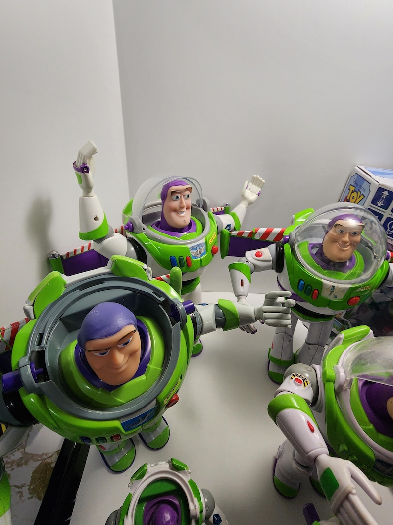 May include: A collection of five green, white, and purple Buzz Lightyear action figures from the Toy Story franchise. The figures are all in different poses, with some of them holding their arms out and others with their arms at their sides. The figures are all wearing their signature space ranger suits.