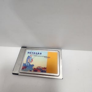 May include: A silver Netgear Network Card for Notebook PC FA 410+ card with a cartoon illustration of a person working on a gear.