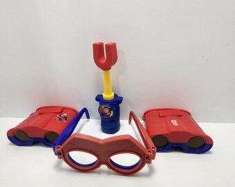 May include: A set of red and blue plastic toy binoculars, a red and blue plastic toy mask, and a red and yellow plastic toy with a blue handle. The toy has a picture of a cartoon character on it.