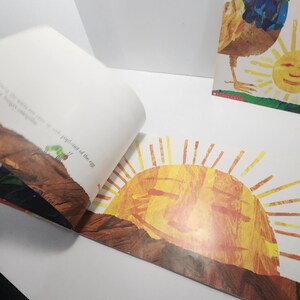 Puede incluir: Un libro infantil abierto con una ilustraci&oacute;n colorida de un sol sonriente que sale sobre una colina marr&oacute;n. El texto en la p&aacute;gina dice "...out of the egg..."