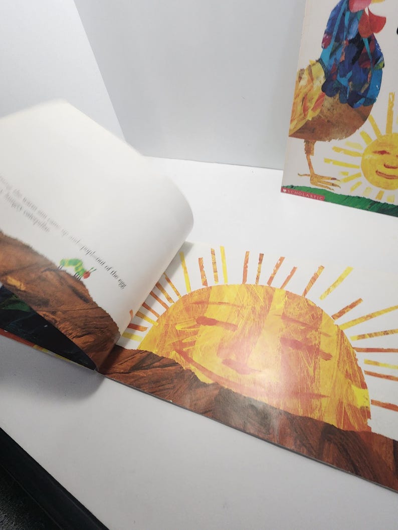 Puede incluir: Un libro infantil abierto con una ilustraci&oacute;n colorida de un sol sonriente que sale sobre una colina marr&oacute;n. El texto en la p&aacute;gina dice "...out of the egg..."