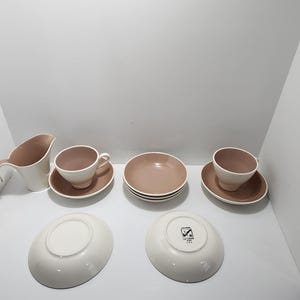 Könnte beinhalten: Eine Sammlung von modernem Geschirr aus der Mitte des Jahrhunderts in einer neutralen Farbpalette. Das Set umfasst Tassen, Untertassen, Schalen und einen Sahnekännchen. Die Tassen und Schalen haben eine hellbraune Innenseite und eine weiße Außenseite.