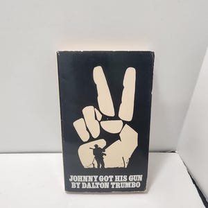 May include: A book cover with a black background featuring a large, off-white peace sign hand gesture. Below the hand is a silhouette of a person holding a rifle. The text "JOHNNY GOT HIS GUN BY DALTON TRUMBO" is printed in white.