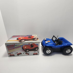 Puede incluir: Un buggy de juguete azul con neumáticos negros y una barra antivuelco. El buggy tiene un diseño de flor en la parte delantera y está junto a una caja con las palabras "Triple Buggy" y "Culbutant". La caja muestra un buggy rojo.