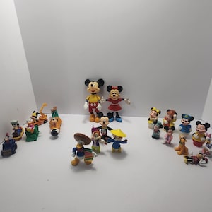 Op de afbeelding: Een verzameling Disney-personagebeeldjes, waaronder Mickey Mouse, Minnie Mouse, Donald Duck en Goofy. De beeldjes zijn felgekleurd en in verschillende poses, sommige dragen hoeden en kostuums. De collectie is gerangschikt op een wit oppervlak.