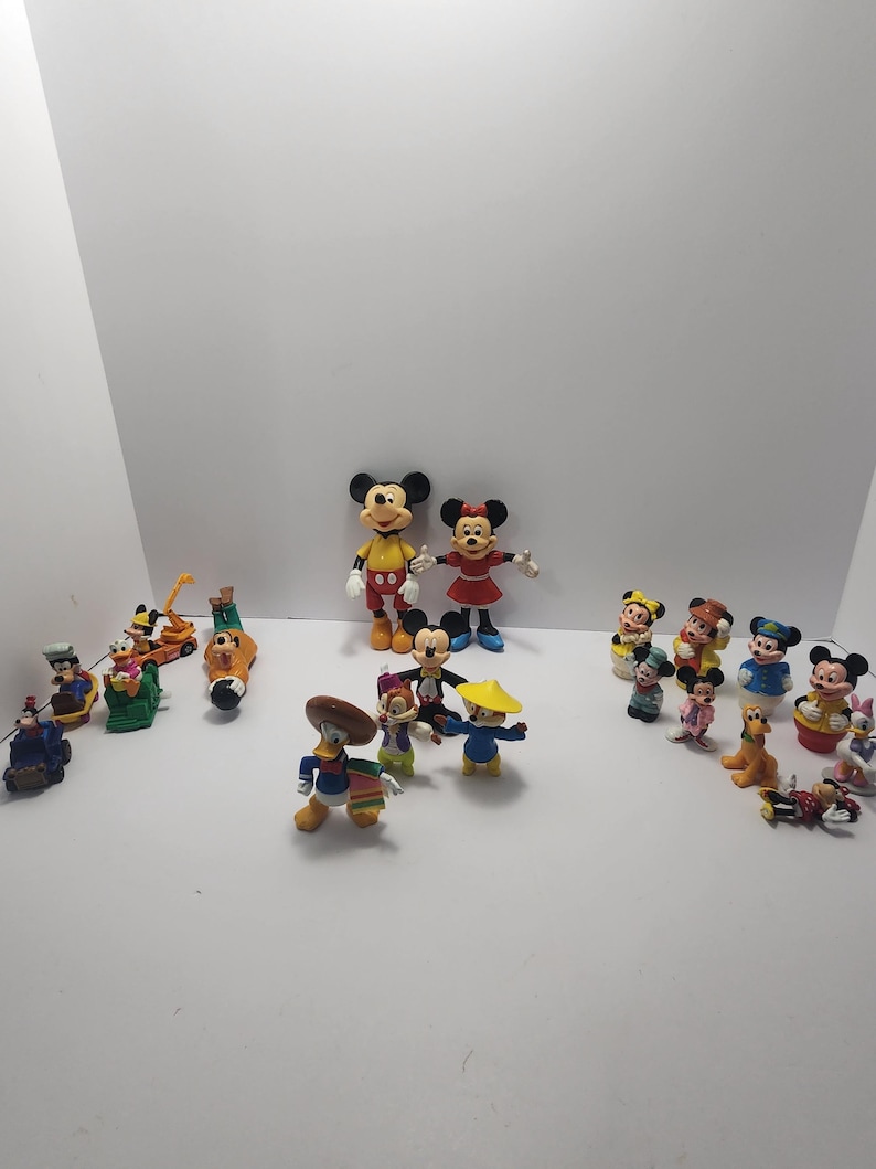 Op de afbeelding: Een verzameling Disney-personagebeeldjes, waaronder Mickey Mouse, Minnie Mouse, Donald Duck en Goofy. De beeldjes zijn felgekleurd en in verschillende poses, sommige dragen hoeden en kostuums. De collectie is gerangschikt op een wit oppervlak.