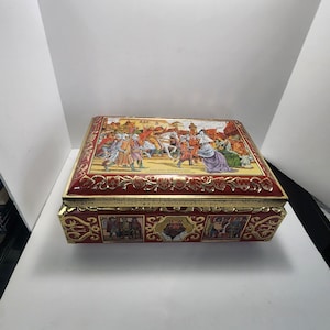 May include: A rectangular, red and gold decorative tin box. The lid features a colourful illustration of a historical scene with figures in period clothing. The box has gold trim and decorative panels around the sides.