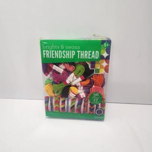 Peut inclure: Une boîte de "brights & neons FRIENDSHIP THREAD" contenant 36 échevettes de 17 couleurs. La boîte est verte et blanche, avec une face transparente montrant des échevettes de fil colorées et des bracelets d'amitié finis. Pour les 6 ans et plus.