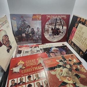 May include: A collection of vintage Christmas-themed vinyl records. Album covers feature festive imagery, including Santa Claus, Christmas trees, and winter scenes. Titles include "Great Songs of Christmas" and "The Statler Brothers Christmas Card."