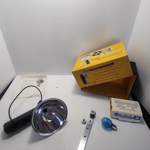 May include: A vintage Kodak Standard Flashholder kit with a yellow box, a chrome reflector, a black handle, and a blue flashbulb. The kit includes a metal bracket, screws, and a small instruction sheet. The box reads "Kodak Standard Flashholder".