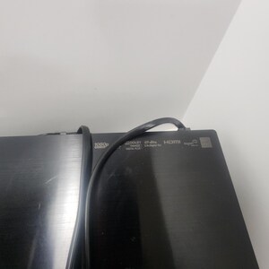 K&ouml;nnte beinhalten: Ein schwarzes elektronisches Ger&auml;t mit einem eingesteckten Stromkabel. Das Ger&auml;t verf&uuml;gt &uuml;ber mehrere Tasten und Beschriftungen, darunter "1080p", "Dolby Digital", "DTS Digital Surround", "HDMI" und "A/V Out".