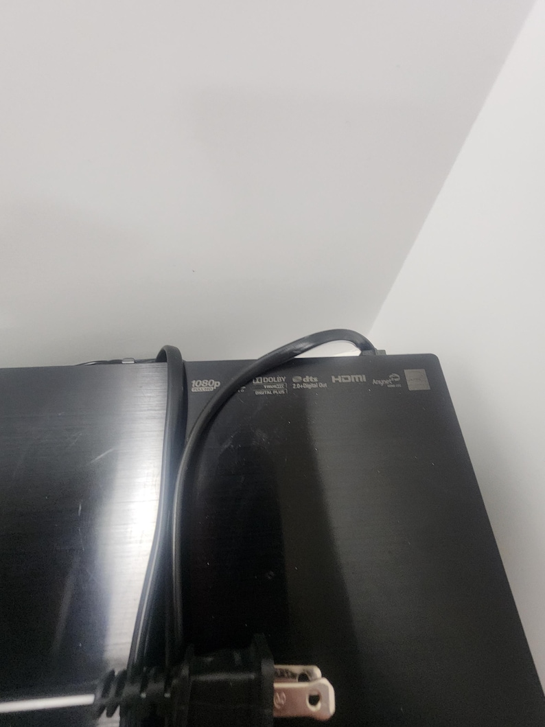 K&ouml;nnte beinhalten: Ein schwarzes elektronisches Ger&auml;t mit einem eingesteckten Stromkabel. Das Ger&auml;t verf&uuml;gt &uuml;ber mehrere Tasten und Beschriftungen, darunter "1080p", "Dolby Digital", "DTS Digital Surround", "HDMI" und "A/V Out".