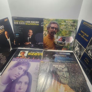 Puede incluir: Una colección de discos de vinilo vintage con portadas de álbumes que muestran retratos, texto y varios diseños. Los títulos incluyen "Academy Award Songs", "Mozart Horn Concertos" y "King of the Road".