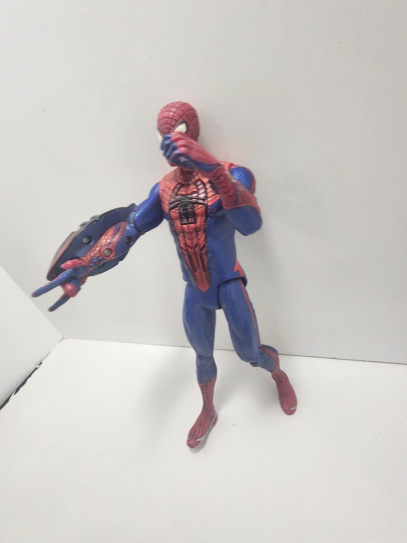 May include: A Spider-Man action figure in a dynamic pose. The figure is mainly blue and red, with a detailed spider-web pattern on the torso and mask. The figure has a web-shooter on the left arm.