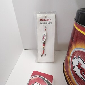 May include: A fishing lure in a clear plastic package with the text "Dictator Spinning Lure". The lure has a white oval body with a red and white logo. The lure has a red hook and red beads.