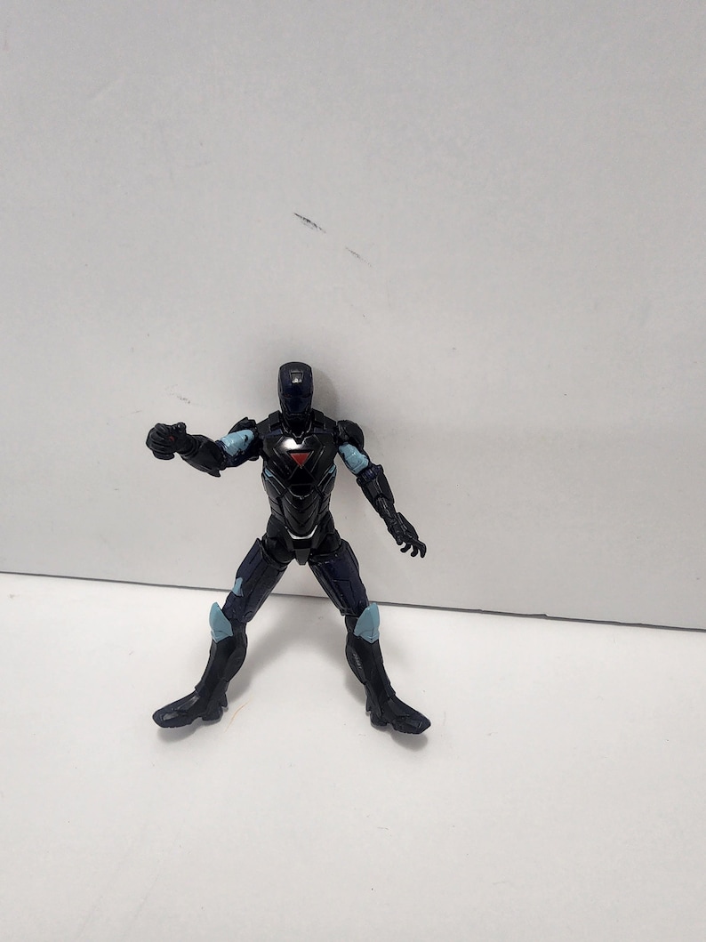 May include: Black and blue action figure of a superhero wearing a helmet and armor. The figure is posed in a fighting stance with one arm raised.