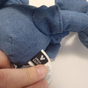Puede incluir: Primer plano de un peluche de mezclilla azul. El juguete tiene una etiqueta que dice "Edici&oacute;n Especial" con el logotipo de Mickey Mouse. El juguete es suave y parece estar hecho de tela de mezclilla.