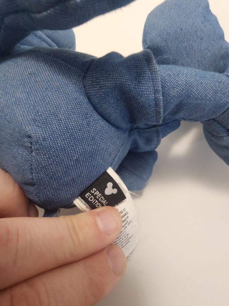 Puede incluir: Primer plano de un peluche de mezclilla azul. El juguete tiene una etiqueta que dice "Edici&oacute;n Especial" con el logotipo de Mickey Mouse. El juguete es suave y parece estar hecho de tela de mezclilla.