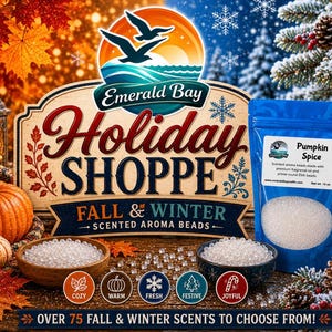 May include: A blue plastic pouch of Pumpkin Spice scented aroma beads with a white label, positioned next to two wooden bowls filled with clear beads. The background features a sign reading Emerald Bay Holiday Shoppe Fall & Winter.