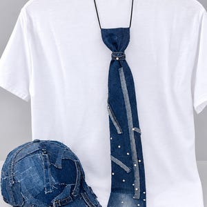 May include: A white t-shirt paired with a dark blue denim necktie featuring frayed edges and scattered white pearl-like embellishments, along with a matching baseball cap constructed from multiple stitched denim patches with frayed seams.