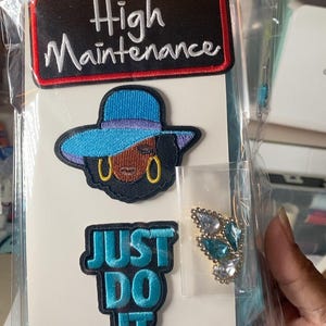 May include: A set of three embroidered patches and one rhinestone embellishment on a white card. The top patch is black with a red border and the text High Maintenance. The middle patch depicts a person in a blue hat. The bottom patch is blue with the text JUST DO IT. A small bag contains a cluster of blue and clear rhinestones.