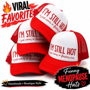 May include: A stack of red and white trucker hats. The hats have a white front panel with the text "I'M STILL HOT it just comes in flashes now". The red brim and mesh back contrast with the white front. The image also includes the text "Funny Menopause Hats".