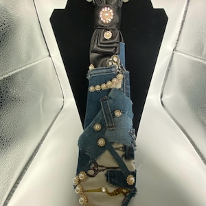 May include: A necktie crafted from black satin and blue denim fabric patches. The tie features a black satin knot adorned with rhinestones and pearls. The denim section includes layered fabric scraps, pearl embellishments, and printed scissor motifs.