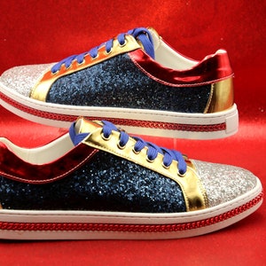 Könnte beinhalten: Ein Paar blaue, rote, goldene und silberne Glitzer-Sneaker mit weißen Sohlen und rotem Besatz. Die Sneaker haben eine weiße und eine blaue Schnürung.