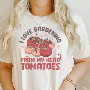 Może przedstawiać: Biały T-shirt z napisem "Uwielbiam ogrodnictwo od głowy do pomidor&oacute;w" w r&oacute;żowych i brązowych literach. Tekst jest otoczony grupą czerwonych pomidor&oacute;w z zielonymi łodygami.