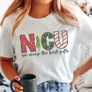 Puede incluir: Una camiseta blanca con un dise&ntilde;o rojo, verde y blanco que dice "NICU we wrap the best gifts".