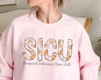 May include: A light pink sweatshirt with the words "SICU" in large, black letters outlined with a floral pattern. The words "Surgical Intensive Care Unit" are written in smaller black letters below the large letters.