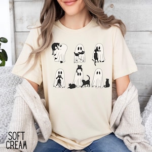 Puede incluir: Una camiseta blanca con un gr&aacute;fico negro de gatos y fantasmas. El gr&aacute;fico muestra seis fantasmas con gatos dentro, fuera y encima de ellos.