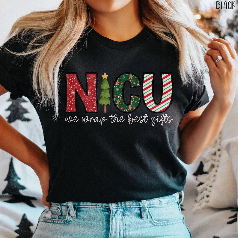 Puede incluir: Camiseta negra con un dise&ntilde;o navide&ntilde;o que dice "NICU we wrap the best gifts". Las letras est&aacute;n decoradas con copos de nieve, bastones de caramelo y un &aacute;rbol de Navidad.
