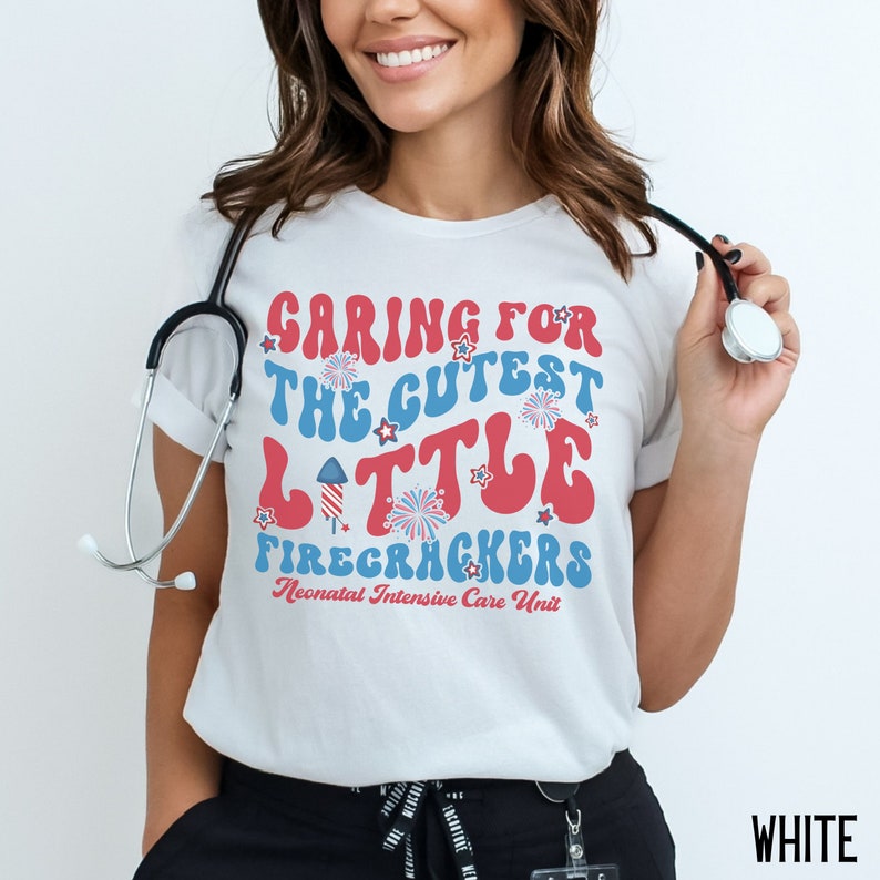 May include: White t-shirt with a red, white, and blue graphic that says "Caring for the Cutest Little Firecrackers Neonatal Intensive Care Unit".
