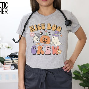 May include: Gray athletic heather t-shirt with a graphic print of a ghost, pumpkin, and spider with the text "Nigh Boo Crew".