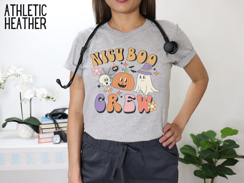 May include: Gray athletic heather t-shirt with a graphic print of a ghost, pumpkin, and spider with the text "Nigh Boo Crew".
