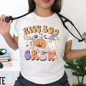 May include: White t-shirt with a retro-style graphic that says "NICU BOO CREW" and features a pumpkin, ghost, and other Halloween-themed imagery.