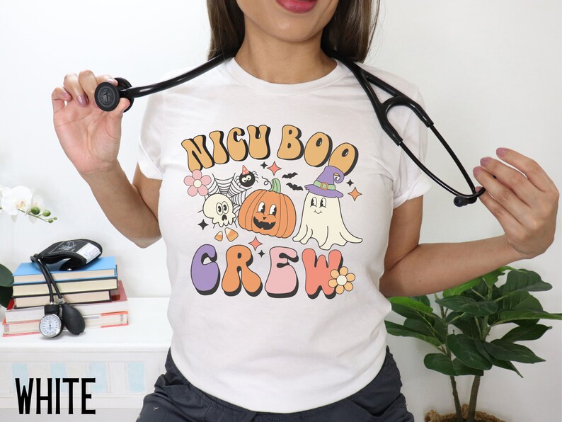 May include: White t-shirt with a retro-style graphic that says "NICU BOO CREW" and features a pumpkin, ghost, and other Halloween-themed imagery.