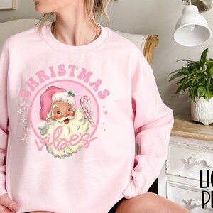 May include: Pink Christmas sweatshirt with a vintage Santa Claus illustration and the text "Christmas Vibes".
