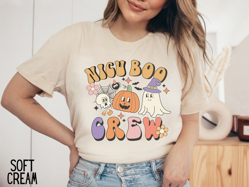 May include: A cream colored t-shirt with a retro-style graphic that says "NIGH BOO CREW" with a pumpkin, ghost, and spider illustration.
