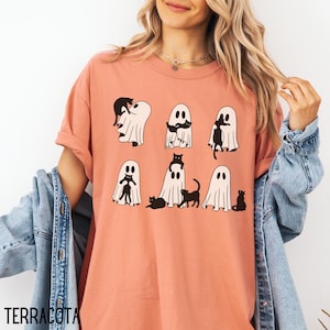 May include: A terracotta colored t-shirt with a graphic of black cats and ghosts. The graphic shows cats hiding inside ghosts. The text "TERRACOTA" is visible at the bottom of the image.