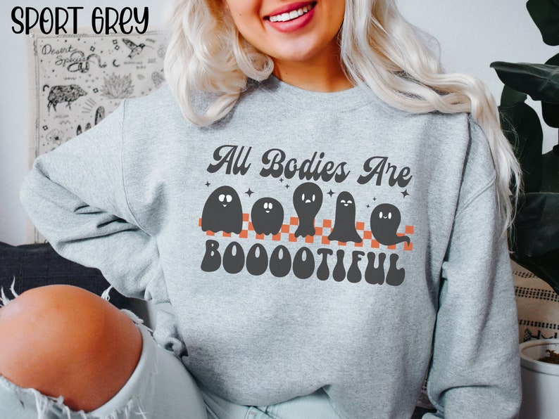 May include: A grey sweatshirt with the text "All Bodies Are Boootiful" in a retro font. The text is surrounded by five black ghosts with orange checkerboard stripes.