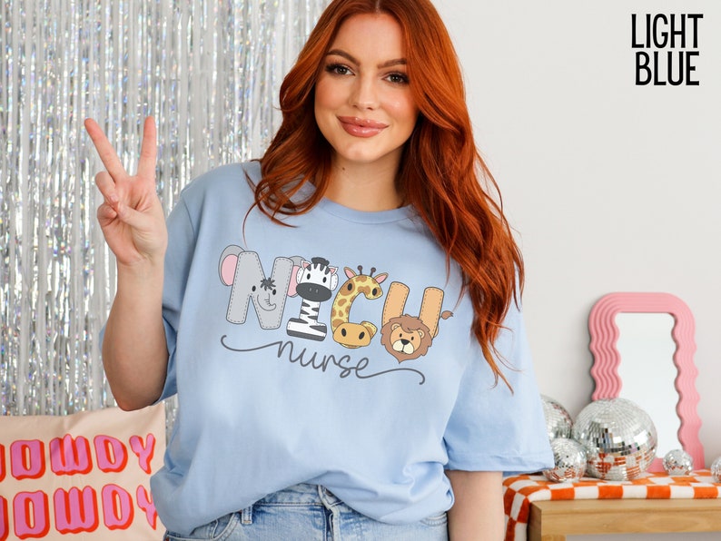 K&ouml;nnte beinhalten: Hellblaues T-Shirt mit einer Grafik von Tieren, die "NICU nurse" buchstabieren.