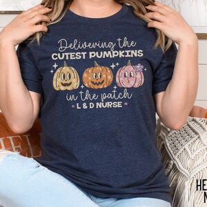 May include: Heather navy t-shirt with the text "Delivering the cutest pumpkins in the patch L&D Nurse". The shirt features three cartoon pumpkins in yellow, orange, and pink.