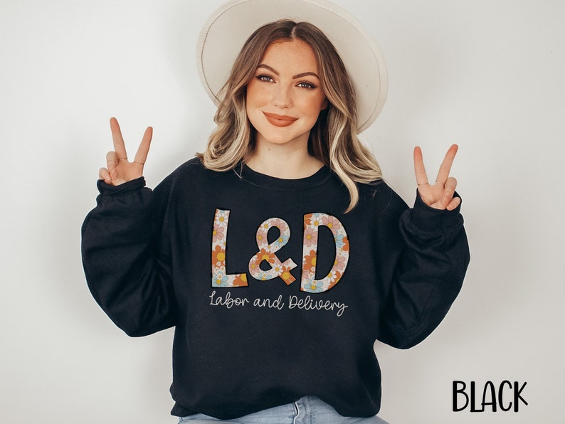 May include: Black sweatshirt with the text "L&D Labor and Delivery" in a floral design. The word "BLACK" is printed in the bottom right corner. The sweatshirt is a crew neck style.