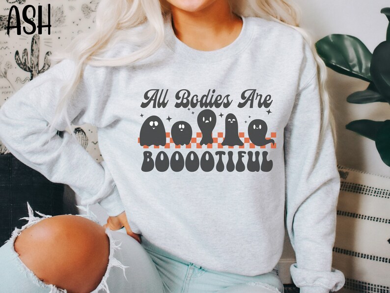May include: A grey sweatshirt with the text "All Bodies Are Boo-o-o-tiful" in a retro font. The text is surrounded by four black ghosts with white eyes and a red and white chequered pattern.