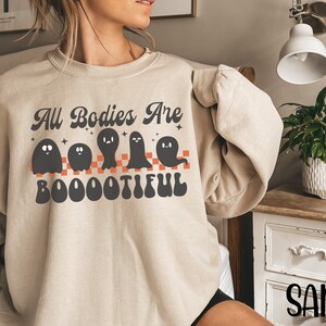May include: A beige sweatshirt with a graphic of ghosts and the text "All Bodies Are Boootiful".