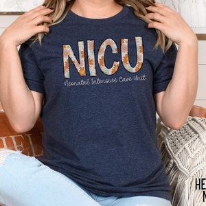 May include: A navy blue t-shirt with a floral design that spells out "NICU" and the text "Neonatal Intensive Care Unit".