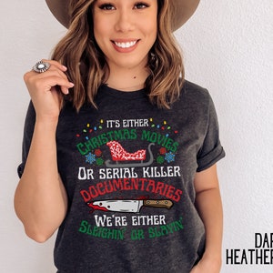 May include: Dark heather gray t-shirt with a Christmas and serial killer themed graphic. The graphic features a red sleigh with a Christmas tree and the text "It's either Christmas movies or serial killer documentaries. We're either sleighin' or slayin'."
